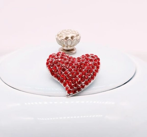 Détail d'une broche en forme de cœur avec strass rouges et monture en alliage argenté
