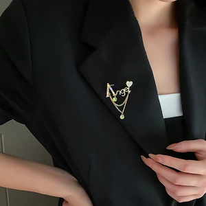 Détail de la broche Angel avec glands dorés et gemmes vertes sur un blazer noir