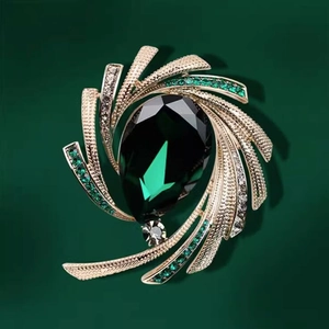 Macro shot of luxury gold brooch with pear-shaped emerald gemstone and green rhinestones