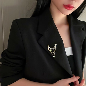 Détail de la broche lettre Angel avec cristaux verts et pompons sur un blazer noir chic