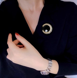 Broche lune dorée avec perles et cristaux portée sur une robe noire à col en V
