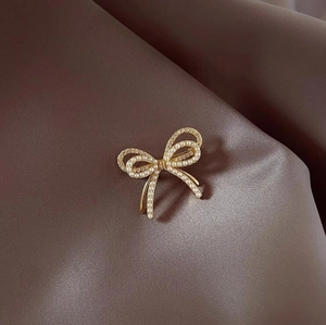 Elegante broche de lazo dorado con perlas blancas y diamantes en fondo de satén marrón
