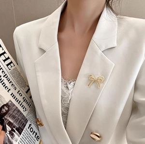 Elegante broche de lazo dorado con perlas en traje blanco, joya para mujer