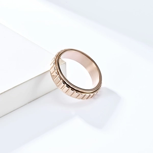 Détail d'une bague rotative or rose avec texture engrenage sur support blanc géométrique