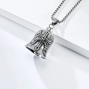 Détail du pendentif cloche en acier avec croix et ailes de plumes sur une chaîne carrée