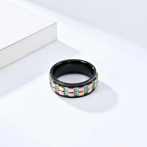 Close-up of matte black spinner ring with rainbow checkered inlay on white geometric stand