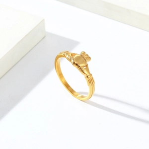 Détail d'une bague Claddagh dorée montrant des mains tenant un cœur couronné sur fond blanc