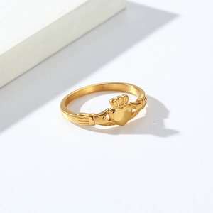 Détail de la bague Claddagh dorée montrant des mains tenant un coeur sur fond blanc