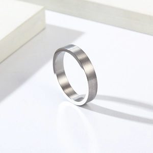 Bague minimaliste de 4 mm en acier titane brossé mat sur un présentoir géométrique blanc
