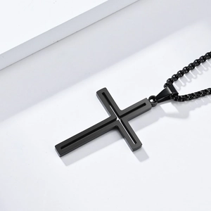 Détail d'un pendentif croix noire évidée avec une chaîne à billes de style épuré