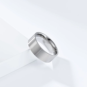 Minimalist silver stainless steel ring with textured horizontal grooves on white geometric stand