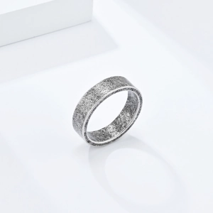 Détail macro d'une bague en titane gris mat de 6 mm sur un socle blanc minimaliste