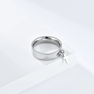 Detail of silver stainless steel ring featuring a hanging cross pendant on a white pedestal