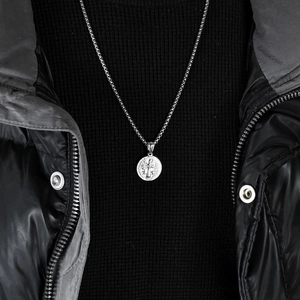 Close-up of Saint Benedict silver pendant with intricate religious relief on a steel chain