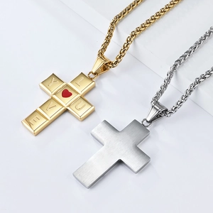 Détail macro de pendentifs croix or et argent avec gravure LOVE et cœur rouge sur chaîne blé