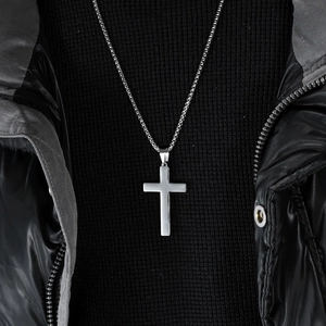 Polished stainless steel cross pendant necklace with silver chain on black knit background