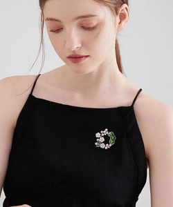 Detail of gardenia flower brooch with green leaves and pearls on a black dress
