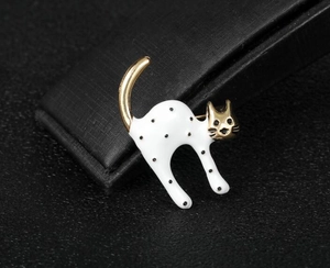 Detailed close-up of a white polka dot cat brooch with gold accents on a black box