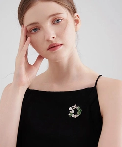 Detail of gardenia brooch with white pearls and green enamel leaves on black fabric