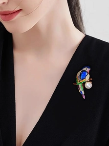 Detailed close-up of parrot brooch with blue rhinestone and pearl on black V-neck top
