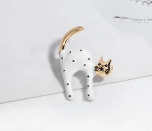 Macro shot of cute cartoon cat brooch with white enamel, black polka dots and gold finish