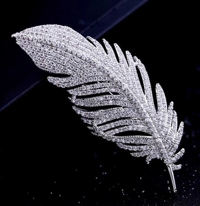 Macro shot of silver feather brooch with sparkling zircons on a dark background