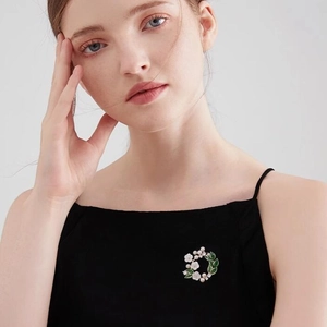 Elegant gardenia brooch with white petals, green leaves, and pearls on a light gold wreath