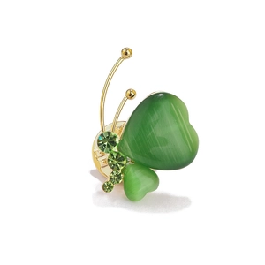 Détail d'une broche papillon dorée avec des ailes en forme de cœur en œil-de-chat vert