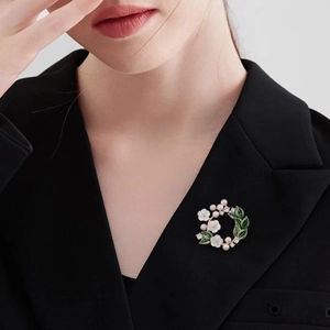 Elegant gardenia brooch with white petals, green enamel leaves, and pearls on a black suit