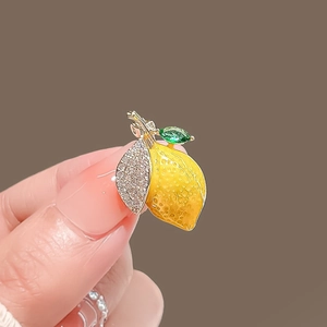 Détail d'une broche citron en émail jaune avec des feuilles en cristal en main