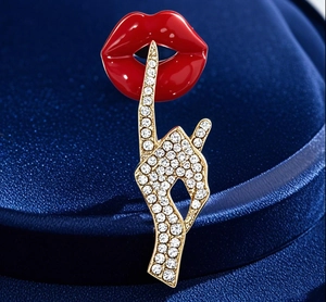Close-up of red enamel lips and gold finger brooch with sparkling white crystals