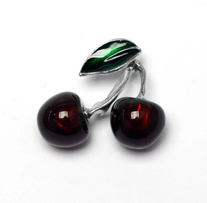 Close-up of sweet cherry brooch with translucent red fruit and green enamel leaf detail