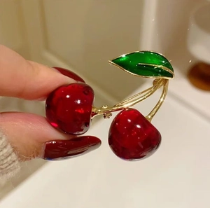 Close-up of sweet cherry brooch with deep red resin fruit and green enamel leaves