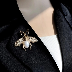 Vue détaillée d'une broche abeille dorée vintage avec perle sur un revers noir