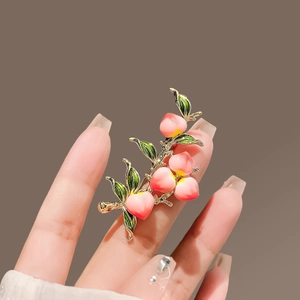 Detailed close-up of a pink enamel peach brooch with green leaves held in hand