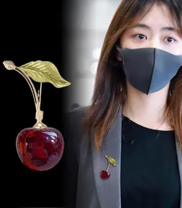 Detailed view of a red cherry brooch with gold leaves on a suit lapel