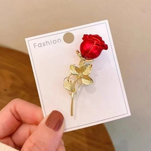 Gros plan d'une broche rose en émail rouge avec feuilles dorées sur carte de mode