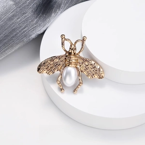 Broche abeille dorée vintage avec perle goutte blanche sur un présentoir blanc chic