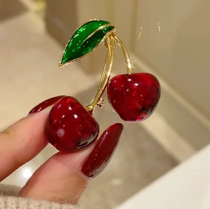 Elegant cherry brooch pin with red resin fruit and golden leaves held by a hand