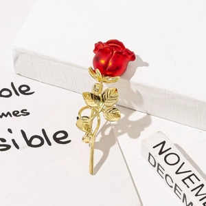Détail d'une élégante broche rose rouge émaillée avec feuilles et tige plaquées or