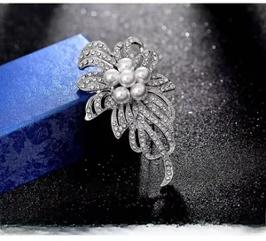 Détail d'une broche fleurie argentée avec perles blanches et feuilles en cristaux