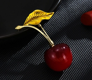 Close-up of elegant cherry brooch with translucent red fruit and golden textured leaves