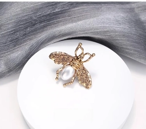 Vue rapprochée d'une broche abeille dorée avec des ailes texturées et une perle