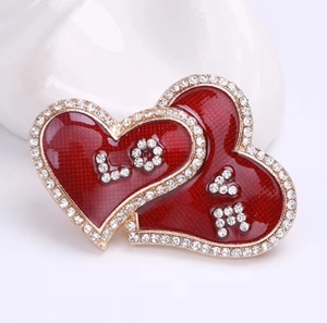 Detailed view of intertwined red enamel heart brooch with LOVE rhinestone lettering