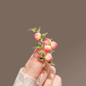 Detailed view of a handmade peach branch brooch with pink enamel and green leaves