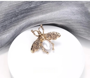 Détail macro d'une broche abeille dorée rétro avec ailes gravées et perle en goutte