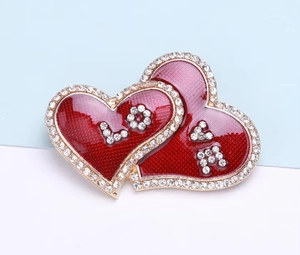 Detailed close-up of a double heart brooch with red enamel and sparkling crystal love inlay