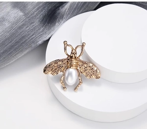 Vue détaillée d'une broche abeille dorée vintage avec perle sur tissu en soie blanche