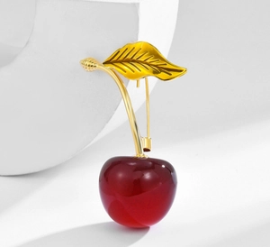 Macro view of realistic red cherry brooch with golden leaves and translucent fruit texture