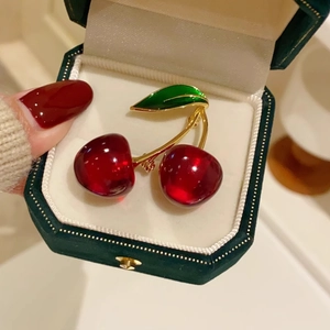 Elegant cherry brooch with red fruit and green leaves in a dark green velvet jewelry box